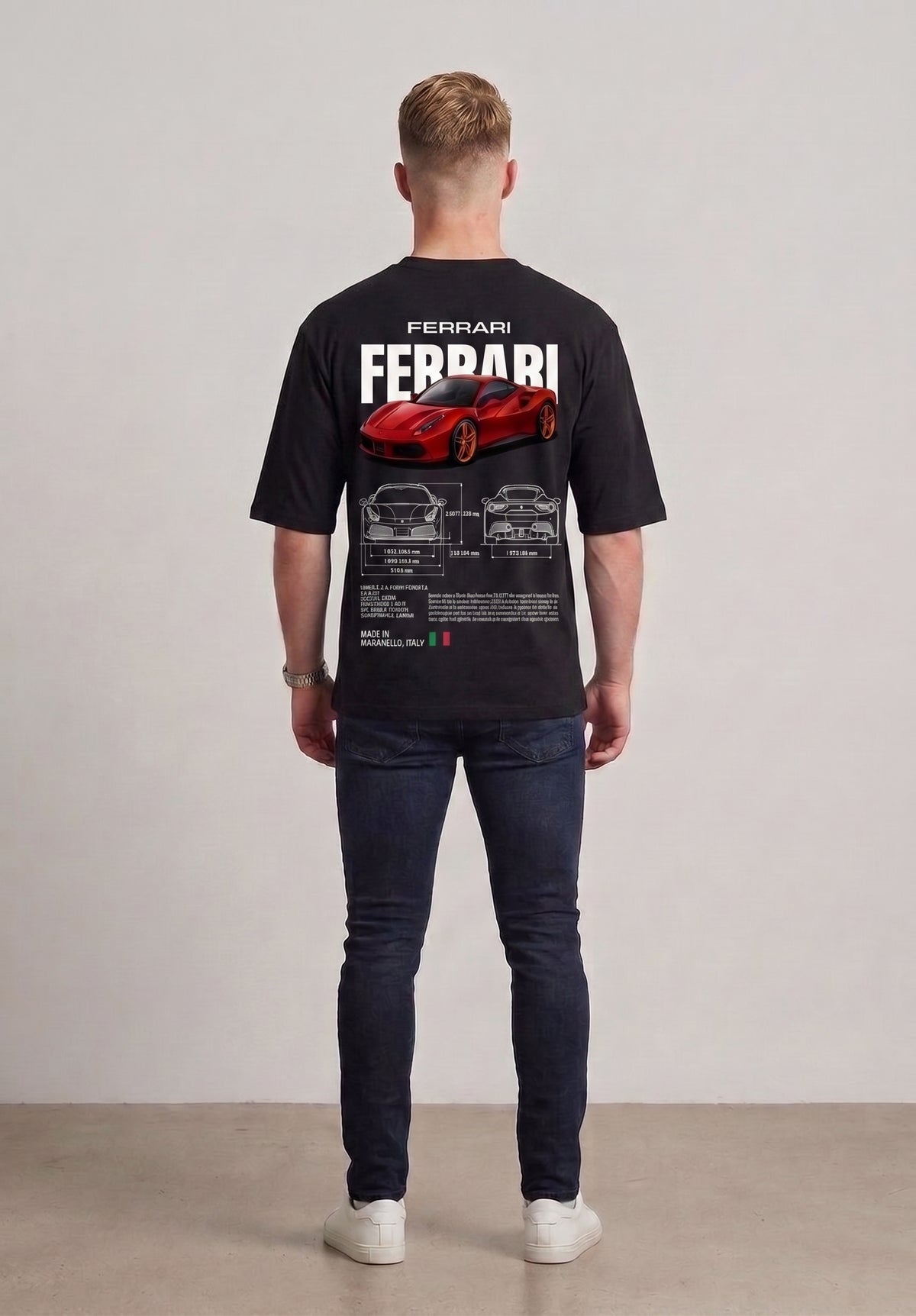 A man viewed from behind wearing a black short-sleeve t-shirt with a large red Ferrari sports car graphic and white 'FERRARI' text on the back, paired with dark blue jeans and white sneakers, against a neutral studio background l AH Urban Wear