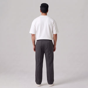 A man viewed from behind wearing a white short-sleeve t-shirt and dark gray baggy  trousers, standing against a light gray studio background l AH Urban Wear