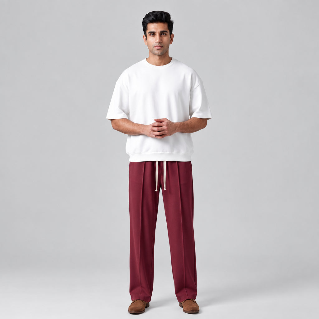 A man stands against a light gray studio background wearing a white crewneck sweatshirt and baggy trouser with brown shoes l AH Urban Wear