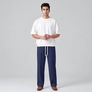 A man modeling a white crewneck sweatshirt and navy blue baggy trouser against a light gray studio background l AH Urban Wear
