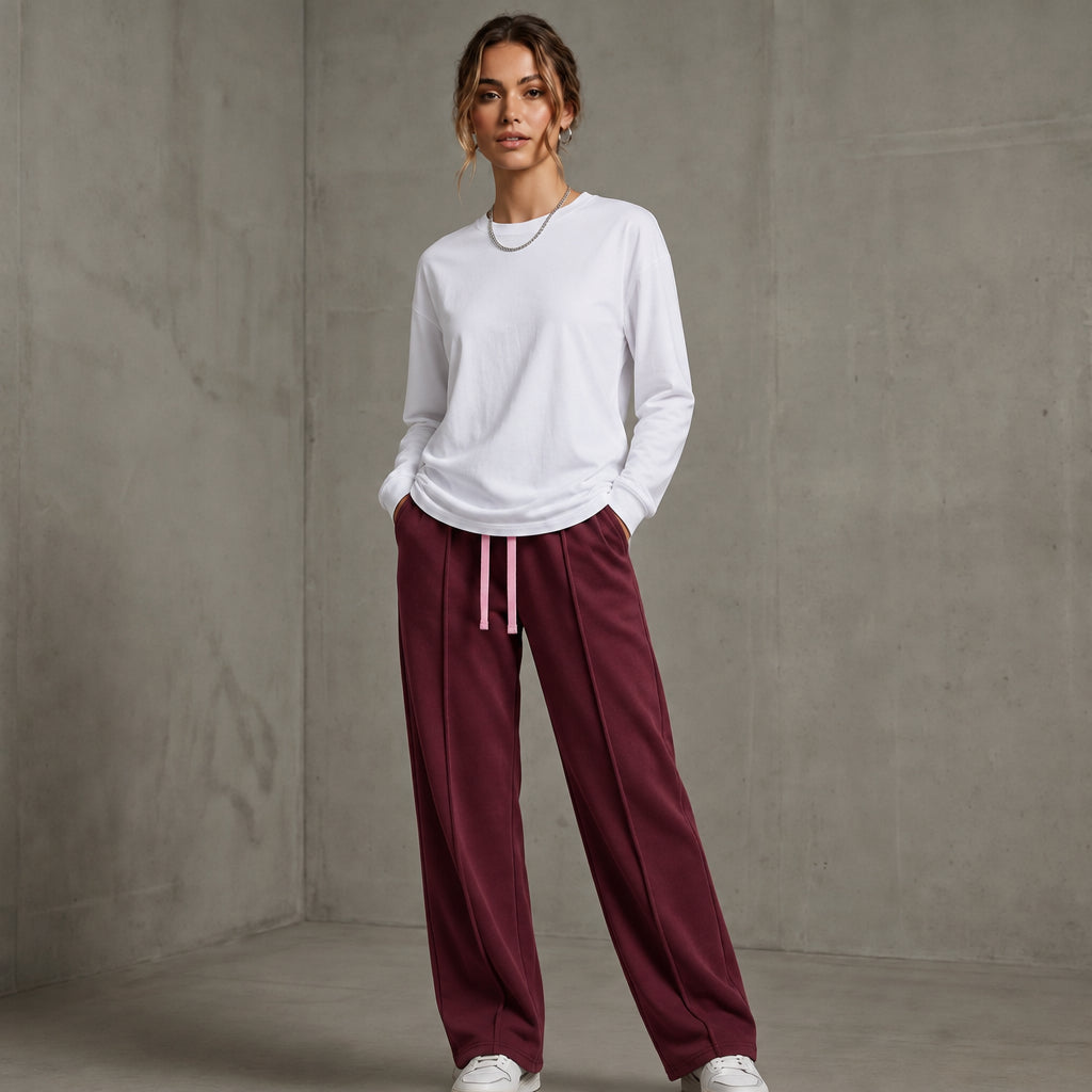 A woman modeling a white full-sleeve t-shirt and maroon baggy trouser against a textured gray concrete wall l AH Urban Wear