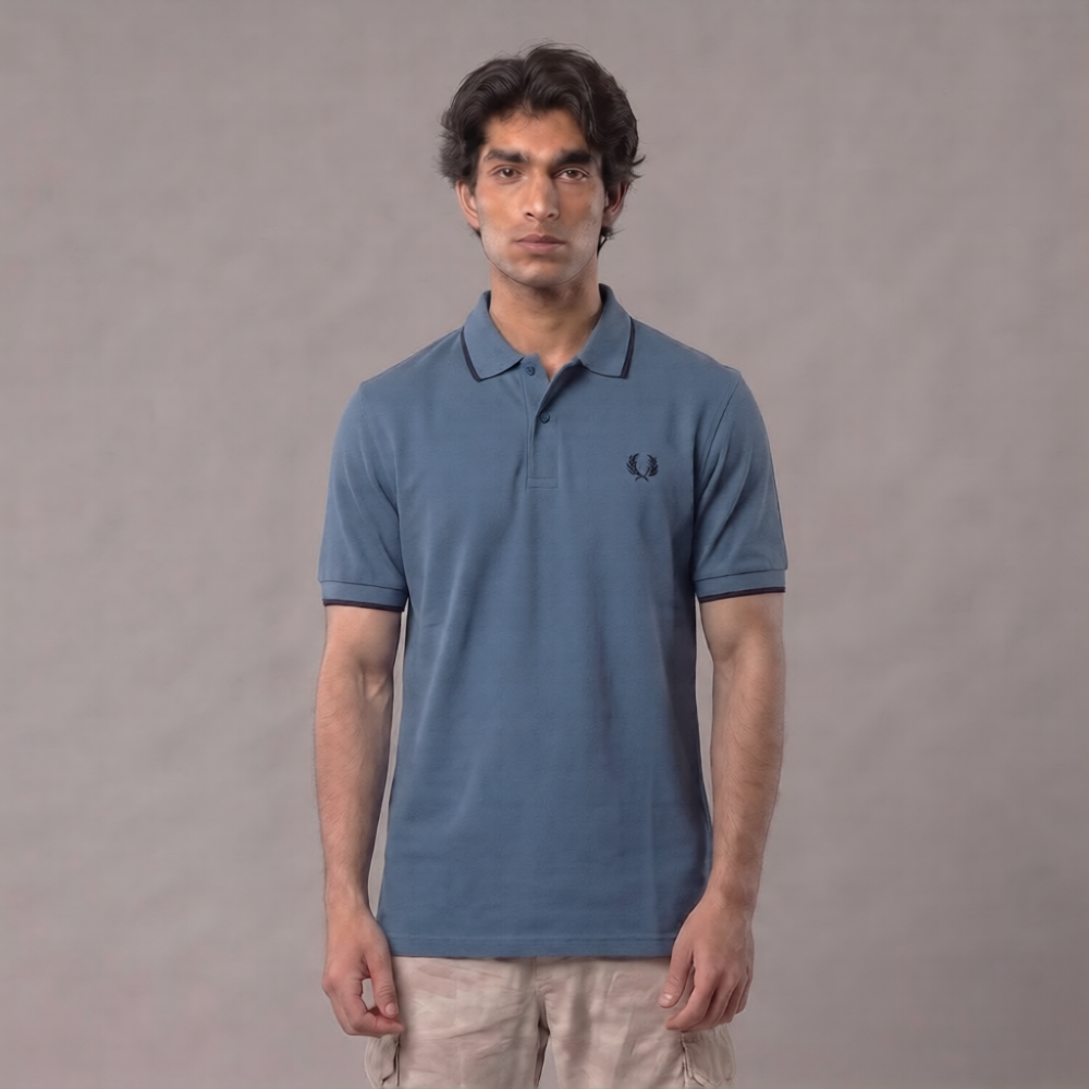 A man wearing a blue short-sleeve polo shirt with a small embroidered logo on the chest, paired with beige pants, standing against a plain gray studio background | AH Urban Wear PK
