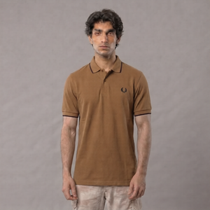 A man wearing a brown short-sleeve polo shirt with black trim and a small embroidered logo on the chest, paired with light beige pants, standing against a neutral gray background | AH Urban Wear PK