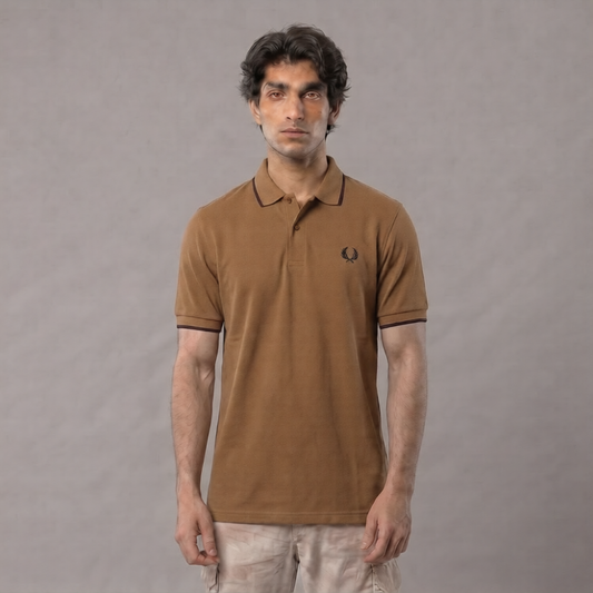 A man wearing a brown short-sleeve polo shirt with black trim and a small embroidered logo on the chest, paired with light beige pants, standing against a neutral gray background | AH Urban Wear PK