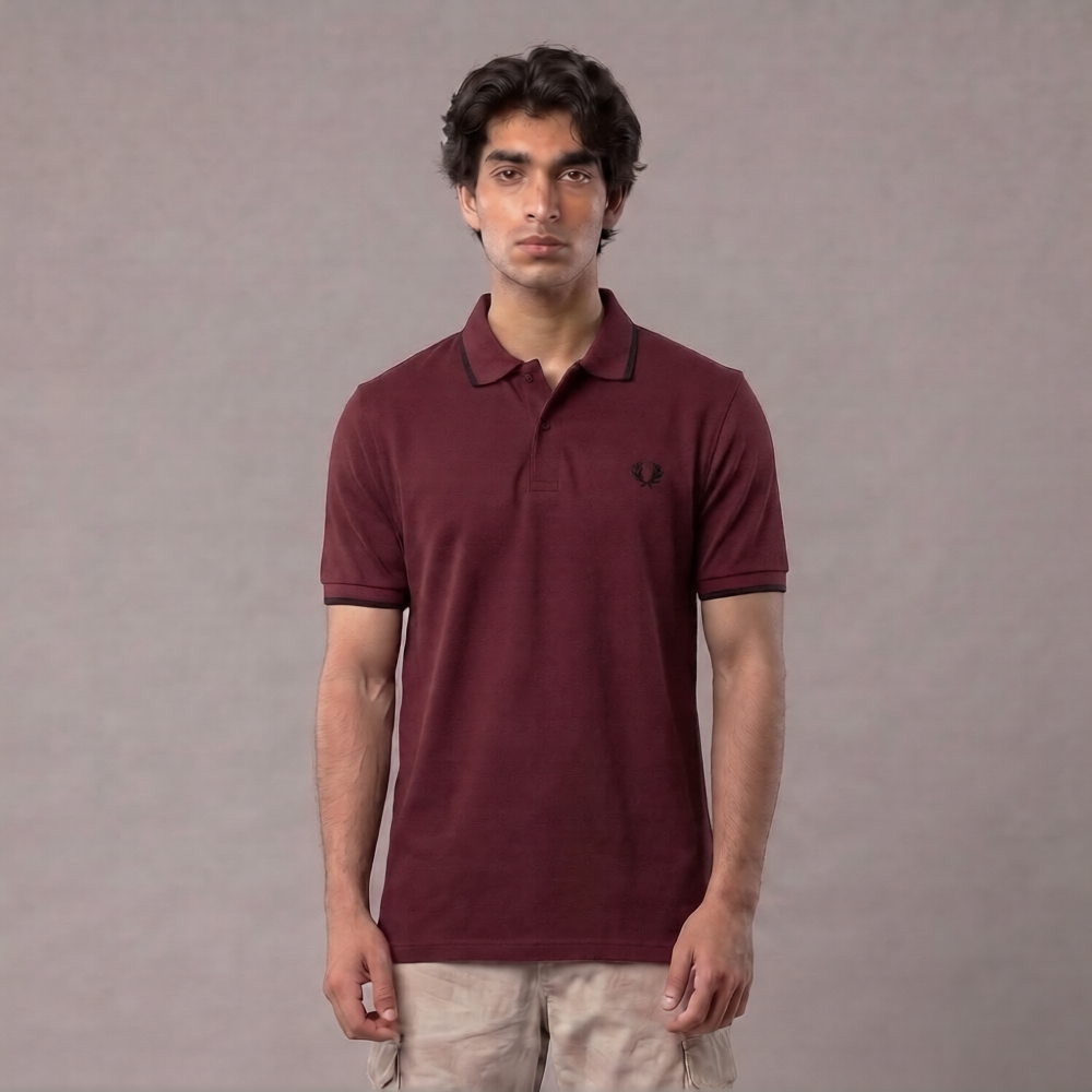 A man wearing a short-sleeve polo shirt in maroon with a small embroidered logo on the chest, paired with light beige pants, standing against a plain gray studio background | AH Urban Wear PK