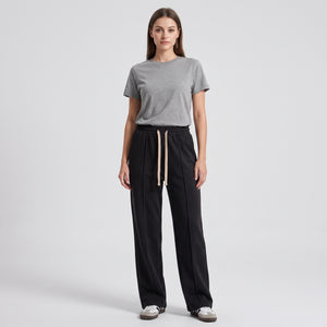 A woman stands against a light gray studio background wearing a heather gray short-sleeve crewneck t-shirt, black baggy trouser, and white sneakers l AH Urban Wear