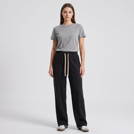 A woman stands against a light gray studio background wearing a heather gray short-sleeve crewneck t-shirt, black baggy trouser, and white sneakers l AH Urban Wear