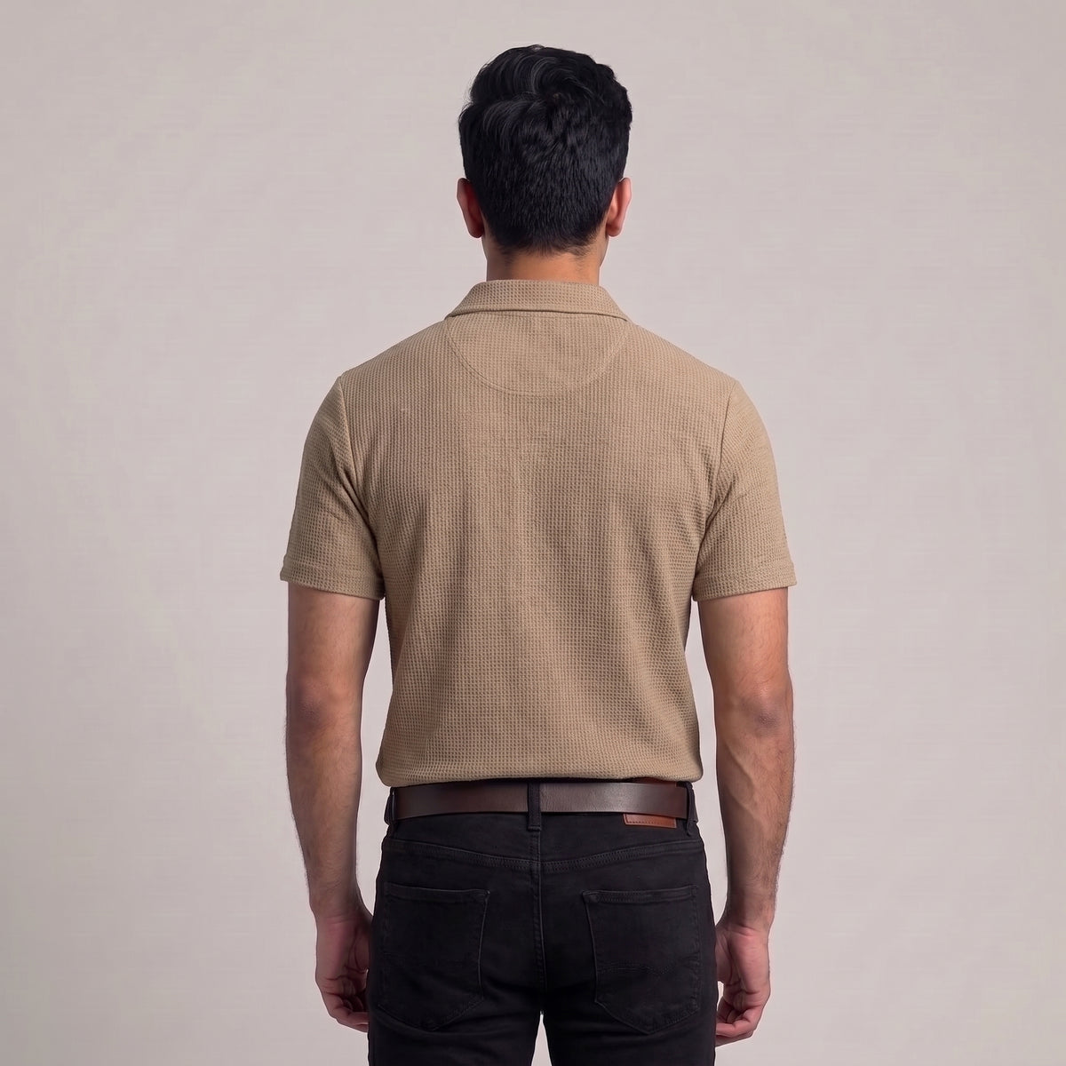 A man viewed from behind wearing a beige short-sleeve textured waffle knit polo shirt and black pants against a plain light gray studio background l AH Urban Wear