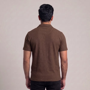 A man viewed from behind wearing a brown short-sleeve polo shirt with a textured waffle knit pattern, paired with black pants, against a plain light beige background l AH Urban Wear