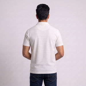 A man viewed from behind wearing a white short-sleeve waffle knit polo shirt and dark blue jeans, standing against a plain light gray studio background l AH Urban Wear