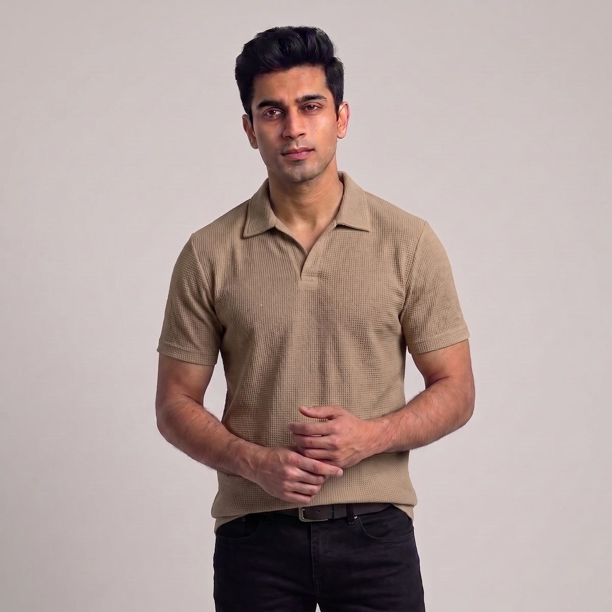 A man wearing a beige short-sleeve polo shirt with a textured waffle knit pattern, paired with black pants, standing against a neutral light gray background l AH Urban Wear