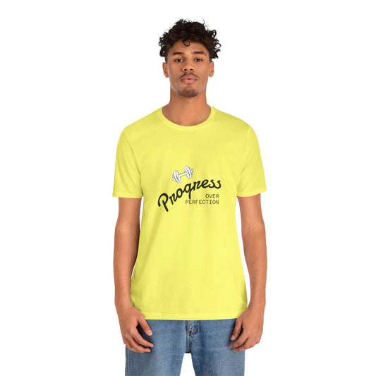 A man wearing a bright yellow t-shirt with a black and white graphic that reads 'Progress OVER PERFECTION' with a dumbbell illustration, paired with blue jeans, against a plain white background | AH Urban Wear PK