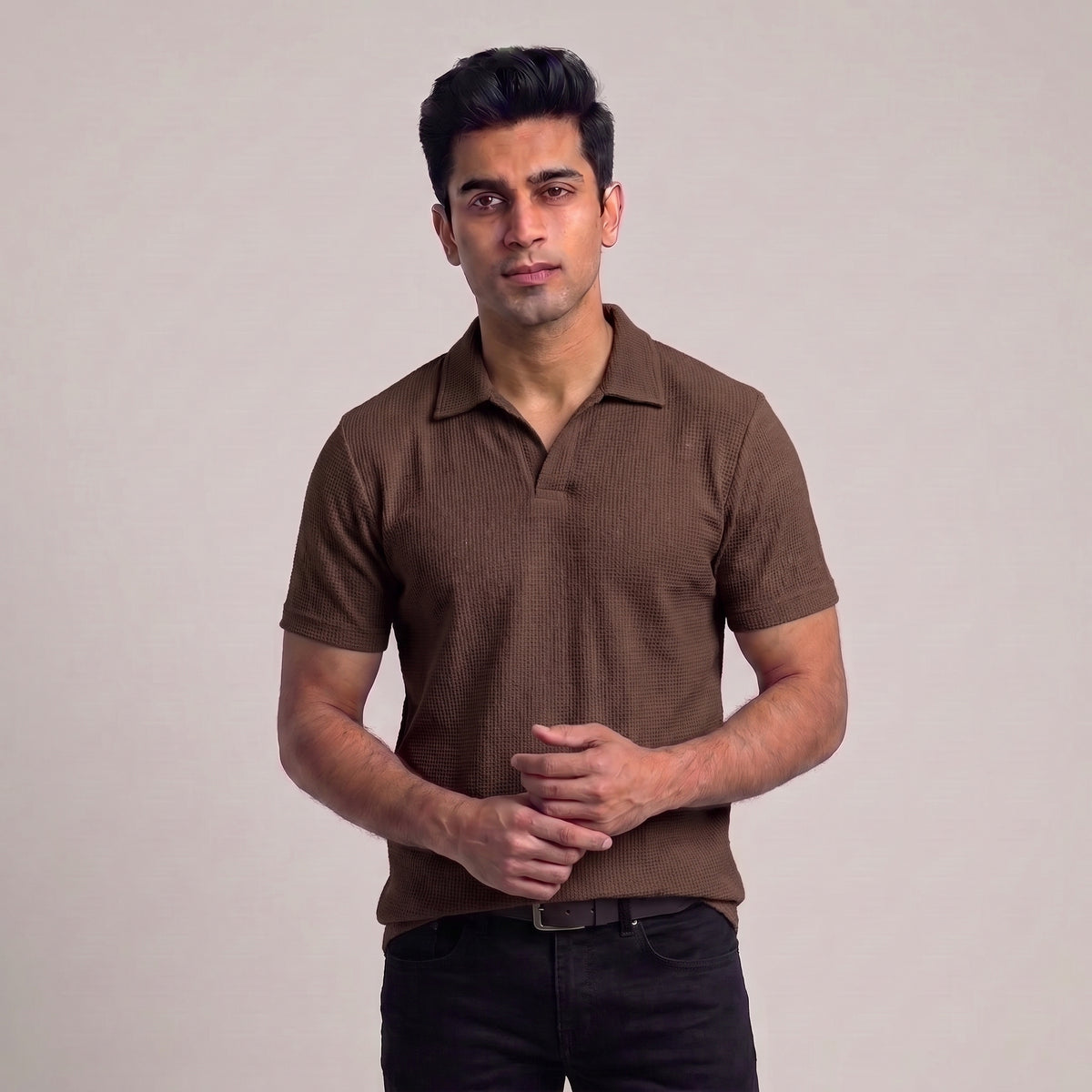 A man wearing a brown short-sleeve waffle knit polo shirt with dark jeans, standing against a plain light gray studio background l AH Urban Wear