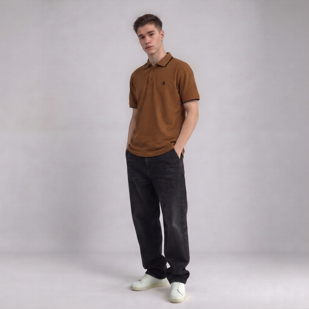 A young man modeling a brown short-sleeve polo shirt with a small embroidered logo on the chest, paired with dark jeans and white sneakers, standing against a neutral gray studio background | AH Urban Wear PK