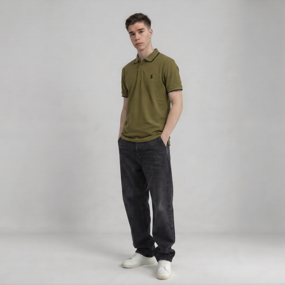 A man modeling an olive green polo shirt with a small embroidered logo on the chest, paired with dark gray jeans and white sneakers, standing against a light gray studio background | AH Urban Wear PK