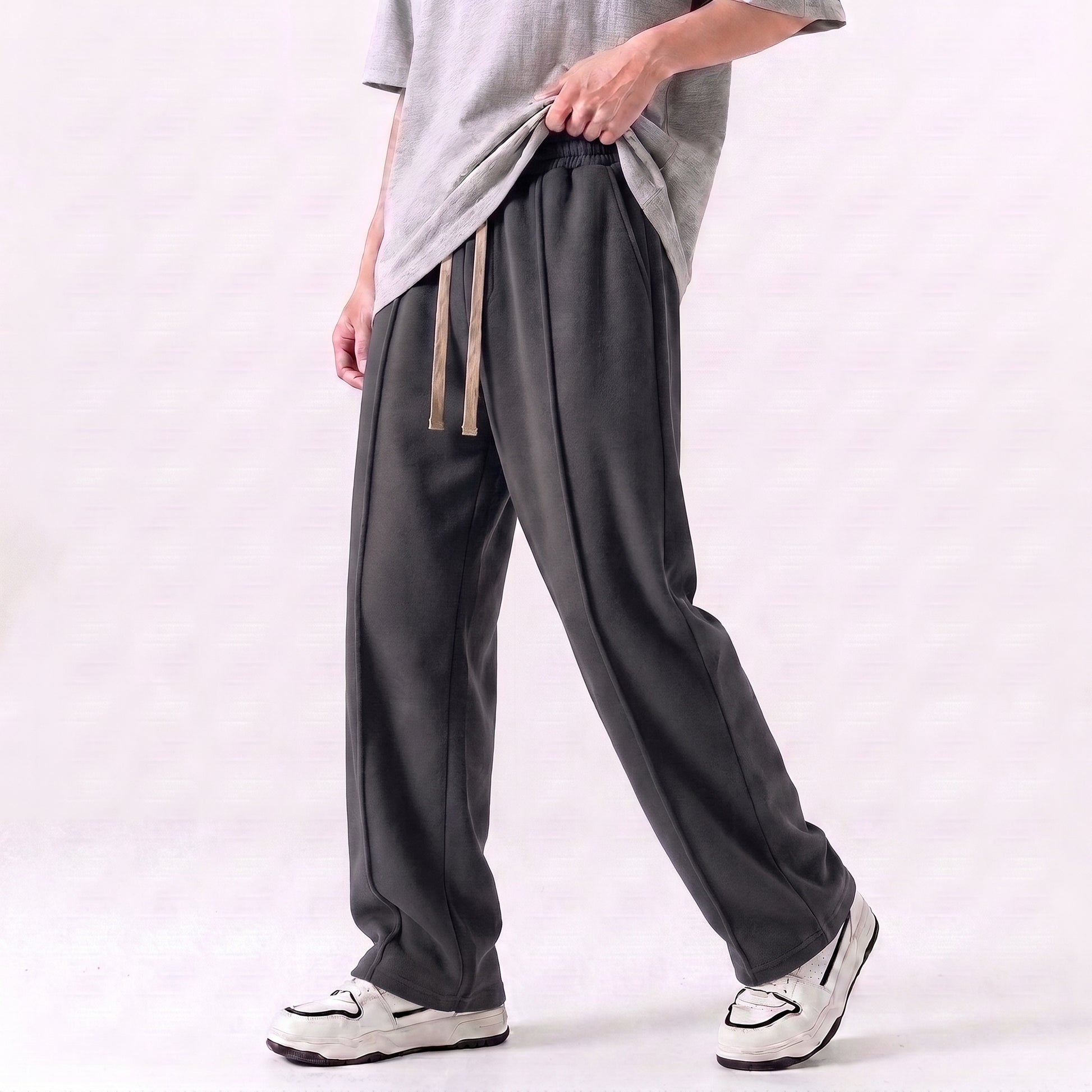 A person wearing loose dark gray drawstring baggy trouser with a light gray T-shirt and white sneakers, shown from the chest down against a plain light background l AH Urban Wear Pk