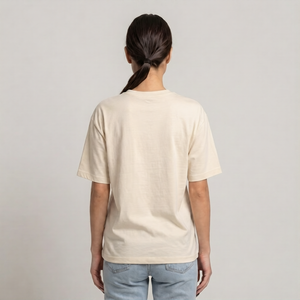 A woman viewed from behind wearing a plain cream-colored drop shoulder t-shirt and light blue jeans against a neutral light gray | AH Urban Wear PKbackground.