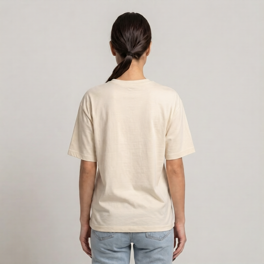 A woman viewed from behind wearing a plain cream-colored drop shoulder t-shirt and light blue jeans against a neutral light gray | AH Urban Wear PKbackground.