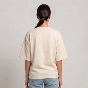 A person viewed from the back wearing an oversized cream-colored short-sleeve t-shirt and light blue jeans, set against a plain light gray studio background l AH Urban Wear