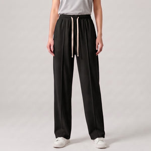 A model wearing black baggy trouser with a light beige cord, paired with a light gray t-shirt and white sneakers, shown from the waist down on a light gray studio background l AH Urban Wear