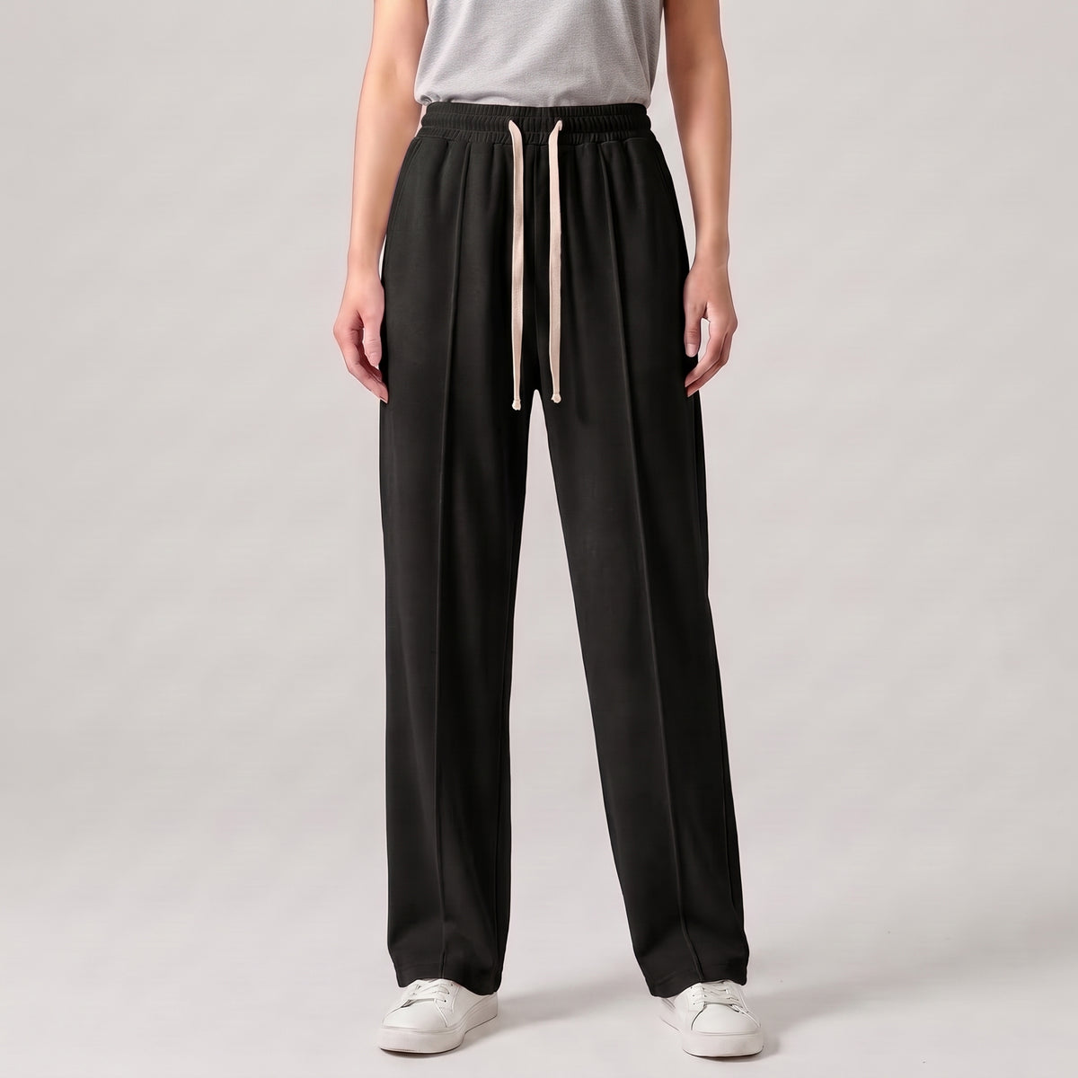 A model wearing black baggy trouser with a light beige cord, paired with a light gray t-shirt and white sneakers, shown from the waist down on a light gray studio background l AH Urban Wear