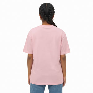 A woman with dark braided hair is shown from the back wearing a light pink drop shoulder t-shirt and light blue jeans against a plain white background.