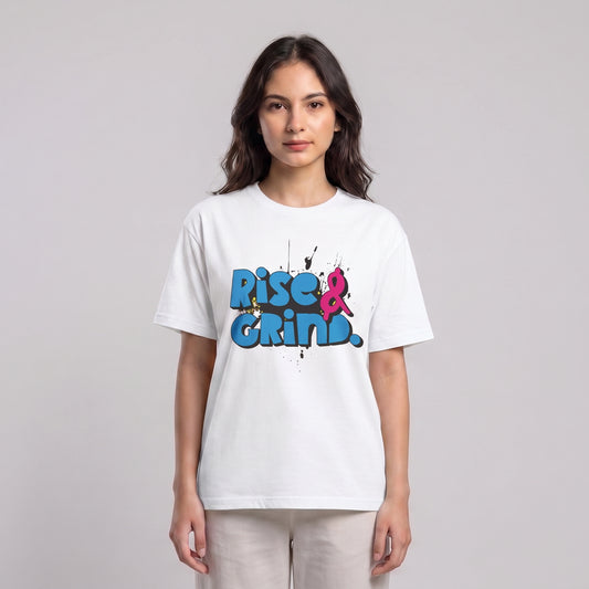 A woman modeling a white short-sleeve t-shirt with a colorful graphic on the chest that reads 'Rise & Grind.' in blue and pink graffiti-style lettering, set against a plain light gray studio background l AH Urban Wear